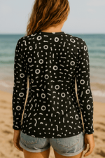 Load image into Gallery viewer, Woman wearing a black and white patterned rash guard on a beach
