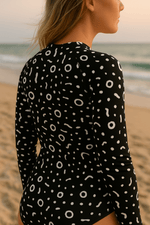Load image into Gallery viewer, Woman wearing a black and white patterned rash guard on a beach
