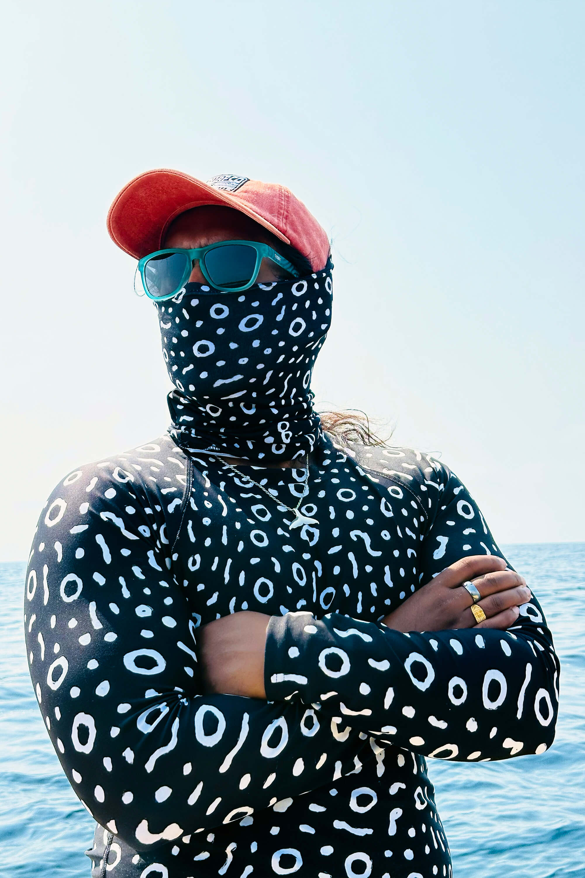 Man wearing an eagle ray patterned rash guard, red cap, and sunglasses with a blue sky background