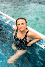 Load image into Gallery viewer, Woman in a black and white patterned swimsuit sitting in a hot tub.

