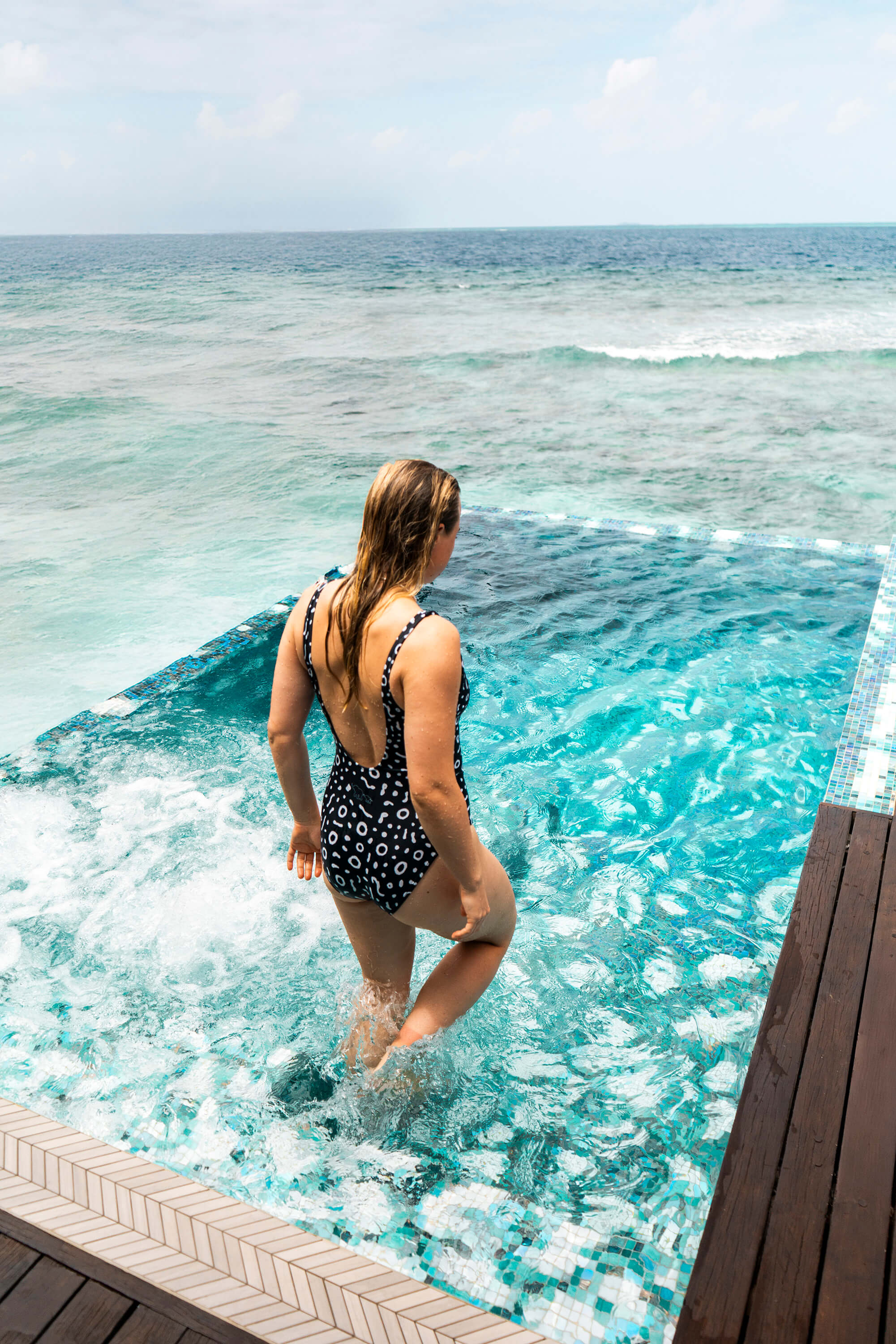 Woman in a swimsuit standing at the edge of a pool overlooking the ocean.