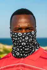 Load image into Gallery viewer, Man wearing a black patterned face cover with ocean and sky in the background
