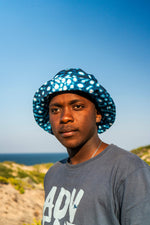 Load image into Gallery viewer, Person wearing a blue patterned hat with a clear blue sky and ocean background
