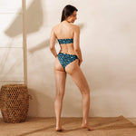 Load image into Gallery viewer, Woman wearing a blue patterned bikini standing against a neutral wall with a woven basket.
